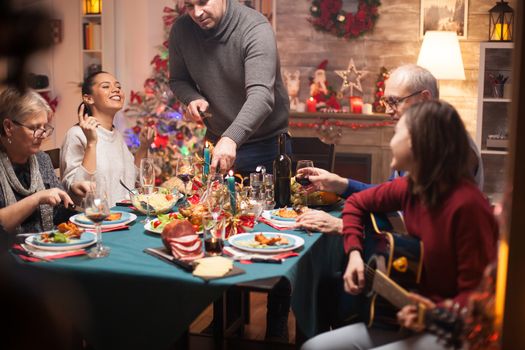 Cheerful mother at christmas family dinner while her daughter is singing on guitar.