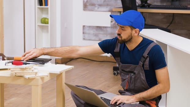 Professional worker checking on laptop for right tools to assembly furniture. Worker wearing a cap.