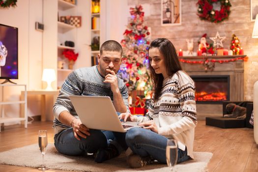 Couple enjoying christmas mood in matching clothes while surfing on laptop.