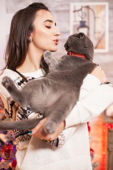 Cheerful young woman trying to kiss her cat on christmas day.