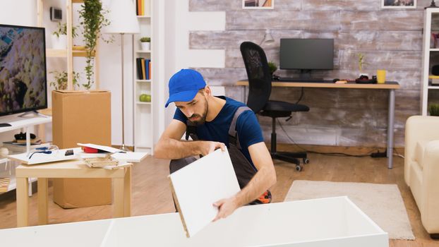 Professional furniture assembly worker wearing a cap while mounting a shelf in new home.