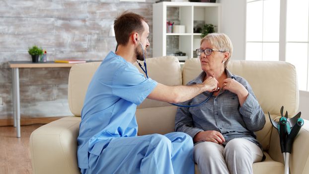 Male doctor putting his stethoscope on and listening old woman heartbeat in nursing home