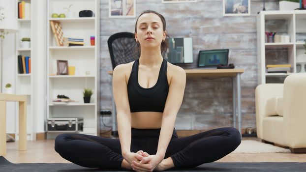 Zoom in shot of beautiful young woman smiling doing yoga meditation in living room.