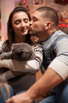 Boyfriend kissing his girlfriend cheek while holding the cat on christmas.