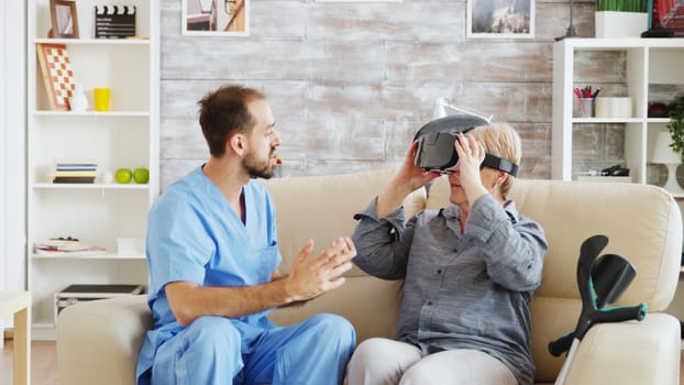 Male doctor in nursing home helping senior woman to use virtual reality goggles