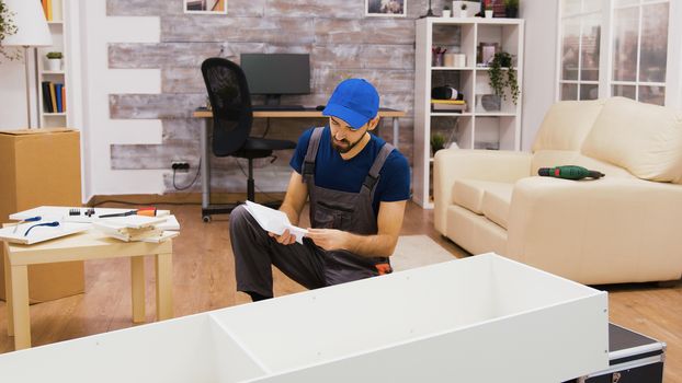 Furniture assembly worker using screwdriver consulting instructions.