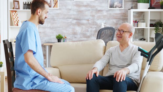 Retired pensioner in nursing home talking with a male nurse in bright and cozy nursing home.