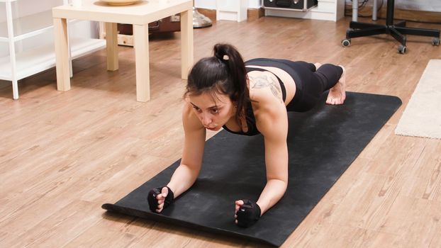 Beautiful caucasian woman training her abs doing plank position in living room.