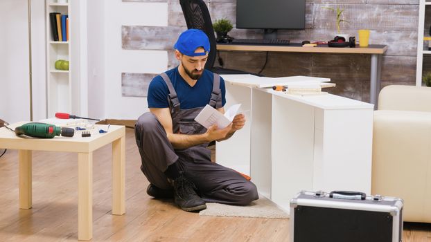 Zoom in shot of man in overalls assembles a shelf and reading instruction.