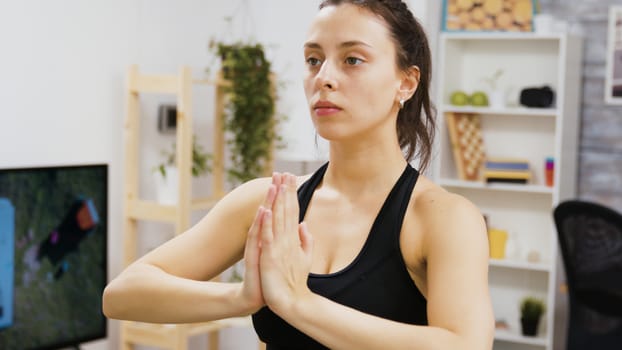 Concentrated young woman relaxing doing yoga exercise in living room.