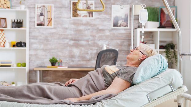 Old lady lying on hospital bed in nursing home. Bright and cozy room