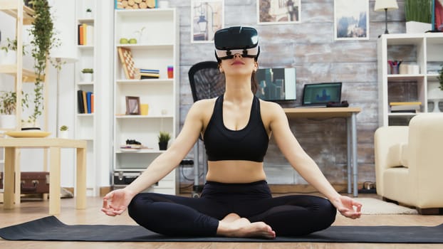 Beautiful young woman wearing virtual reality glasses doing yoga meditation in living room.