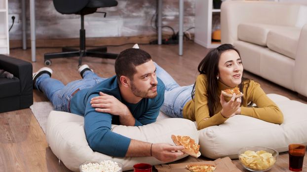 Cat sleeping while her owners are watching tv and eating pizza. Couple sitting on the floor.