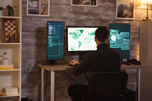 Back view of young hacker sitting on desk writing a malware for cyberterrorism.