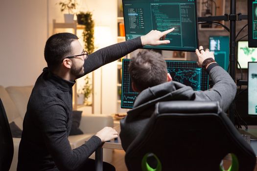 Back view of hackers pointing on computer screens. Dangerous terrorists.