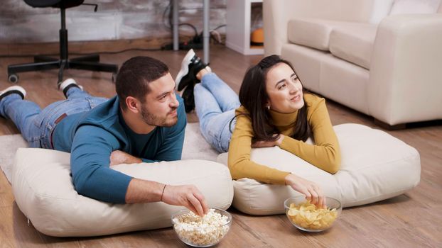 Young woman smiling at his boyfriend while watching tv sitting on the floor.