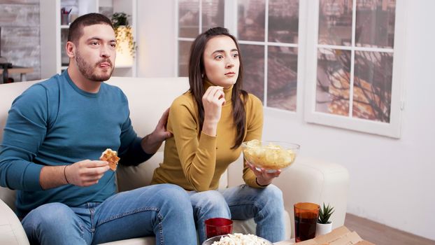 Scared couple after a frightening moment in the movie from tv. Couple sitting on couch eating pizza.