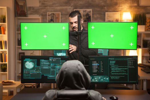 Back view team of hackers doying cyber attacks in front of computer with green screens.