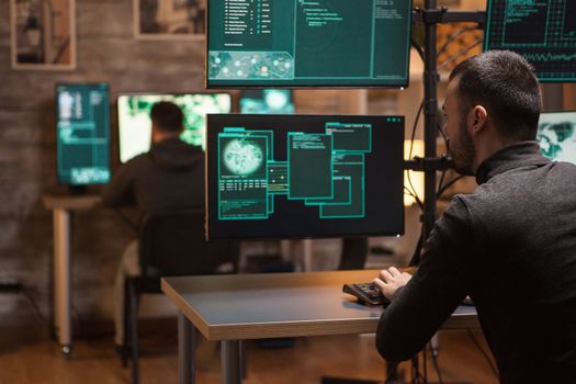 Back view of hackers working on making a dangerous malware on computers with multiple screens.