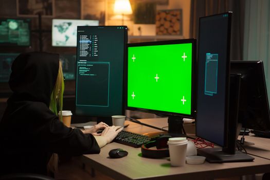 Female hacker wearing a hoodie in front of computer with green screen.