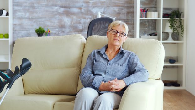 Lonely old woman sitting on couch in a nurshing home keeping hands together