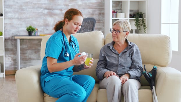 Female doctor sitting on sofa with senior woman in nursing home giving her daily pills.