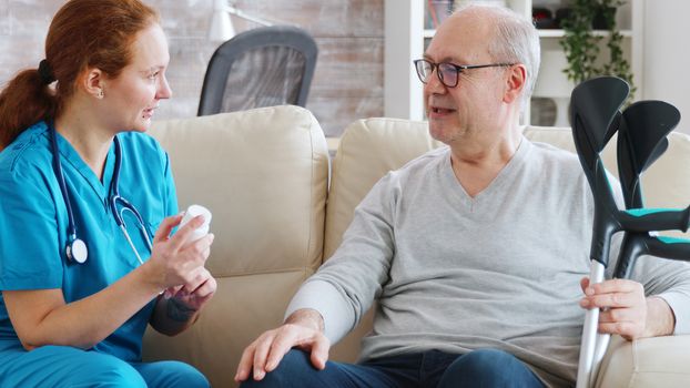 In retirement home nurse is talking with elderly man about drugs dosage. Caregiver and social worker