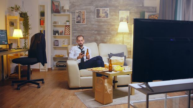 Young businessman in suit and tie relaxing drinking beer and browsing on phone after a hard day at work,