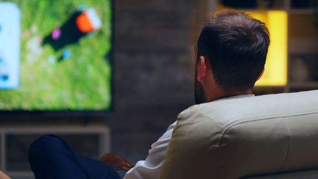 Back view of businessman taking a sip of beer while watching tv.