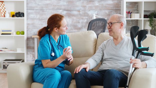 In retirement home nurse is talking with elderly man about drugs dosage. Caregiver and social worker