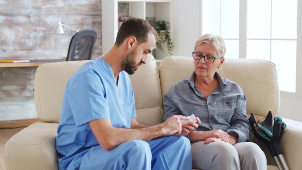 Male nurse sitting on couch with senior woman giving her medical treatment in nursing home.