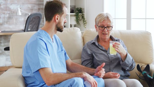 Male nurse sitting on couch with senior woman giving her medical treatment in nursing home.