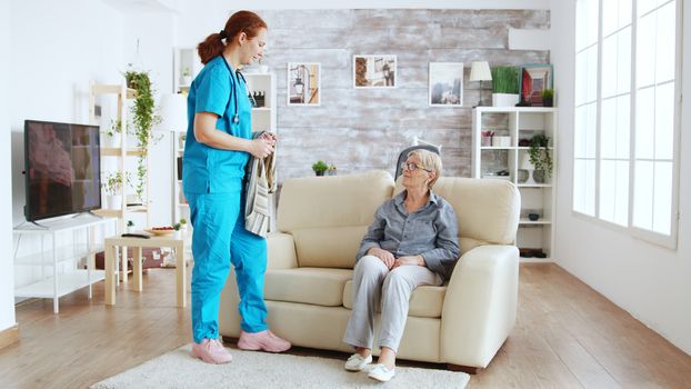 Female nurse helping senior woman getting dressed in nursing home