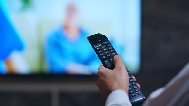 Back view of businessman using tv remote control sitting on couch in his home.