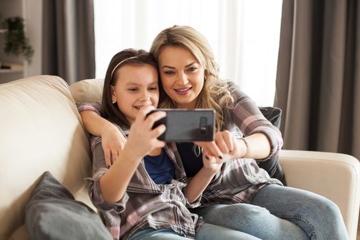 Modern parenting of young mother with her little daughter using smartphone.