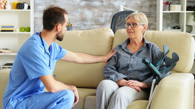 Male nurse talking with old woman suffering of parkinson in nursing home