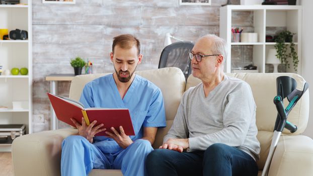 Social worker reading a book to an old disabled man in nursing home.