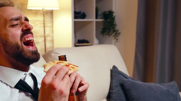 Close up of young entrepreneur laughing while watching tv and drinking beer.