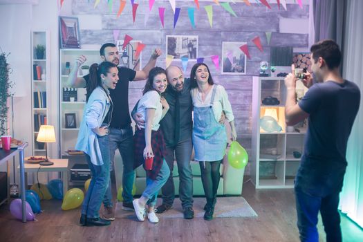 Man taking photos of friends laughing at a party in an apartment.