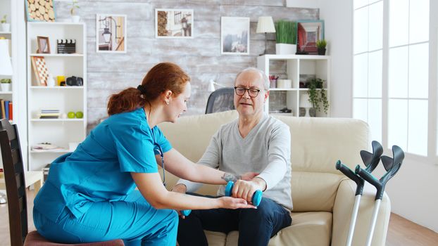 Female nurse helps an old man to make his morning exercises in bright and cozy retirement home