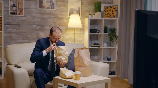 Hungry businessman in suit arriving home with food in paper bag.