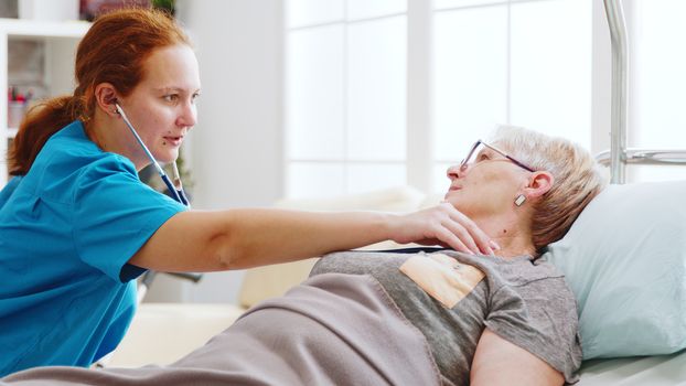 Old lady getting her heartbeats checked by a female nurse in bright and cozy nursing home