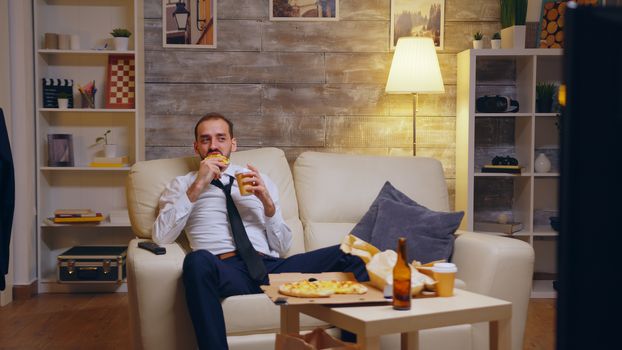 Tired businessman in suit sitting on couch laughing watching tv after a hard day at work.