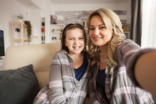 Pov of of little girl with a big smile showing her braces with her mother sitting on the couch.