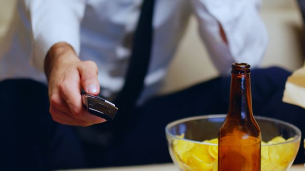 Close up of businessman sitting on couch using remote control. Beer on table.