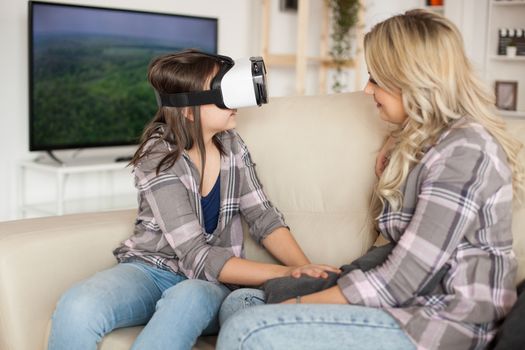 Modern mother looking at her daughter having fun with virtual reality headset.