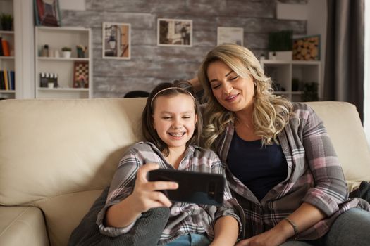 Daughter with braces and her mother watching a video on smartphone.