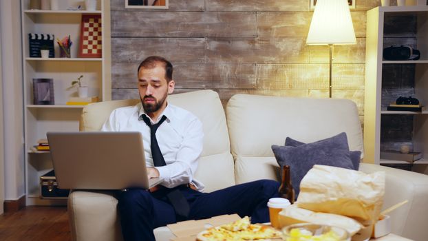 Businessman reaching out for his beer while working on laptop from home. Entrepreneur in suit.