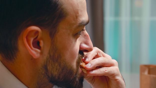 Close up of businessman biting from a burger in living room. Tasty fast food.