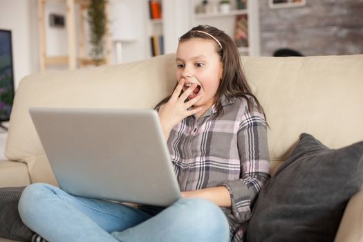Excited little girl with braces while using her laptop sitting on the couch in living room.